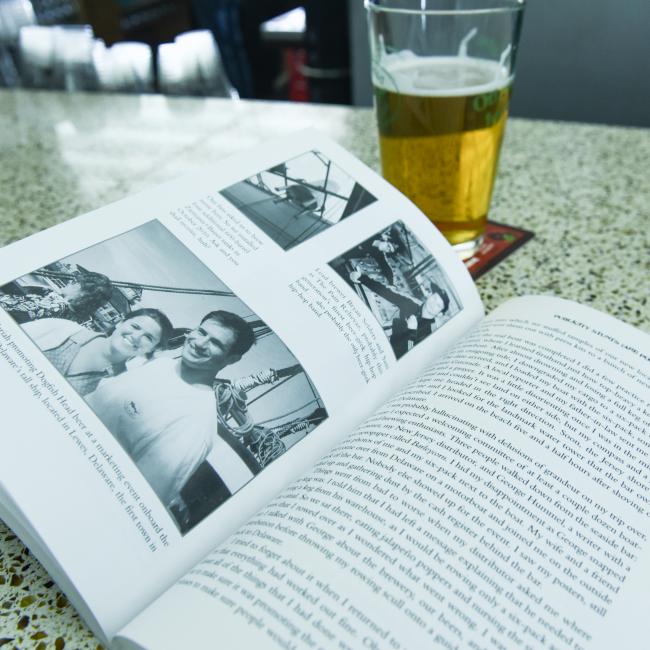 A copy of "Brewing Up A Business" by J Wiley and Sons Publishing rests open on a speckled surface beside a pint of craft beer, creating a relaxed, home-brewing-inspired atmosphere.