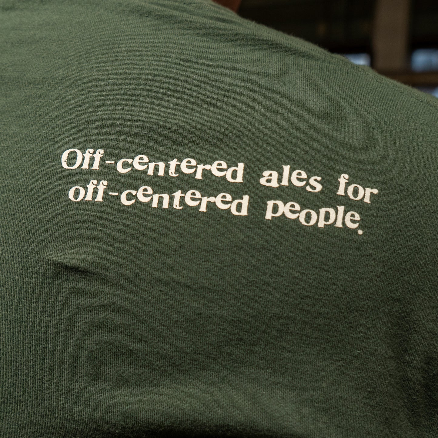 The Green Since 95 Short Sleeve Logo Tee by GO WEST T-SHIRT COMPANY is a soft, green cotton shirt featuring "Off-centered ales for off-centered people" in white text on the back.