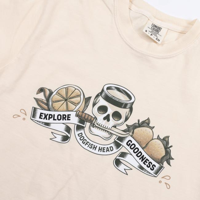 The Ivory Explore Goodness Skull Short Sleeve Tee by GO WEST T-SHIRT COMPANY features a unisex 100% cotton design with a skull, fruit, beer glass, lemon, hops, and a bold EXPLORE DOGFISH HEAD GOODNESS banner—combining comfort and style.