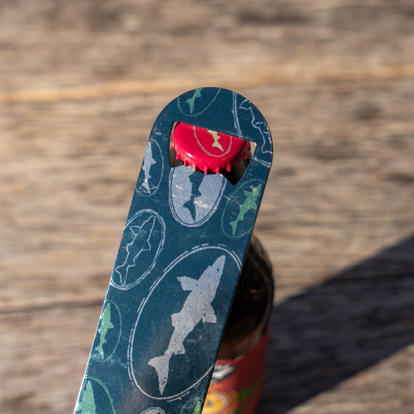 Metal bottle opener with shark design and bottle cap on a wooden surface