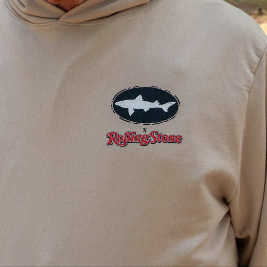Person wearing Dogfish Head x Rolling Stone Mocha Hoodie featuring a black oval Dogfish logo logo a white shark and red Rolling Stone logo