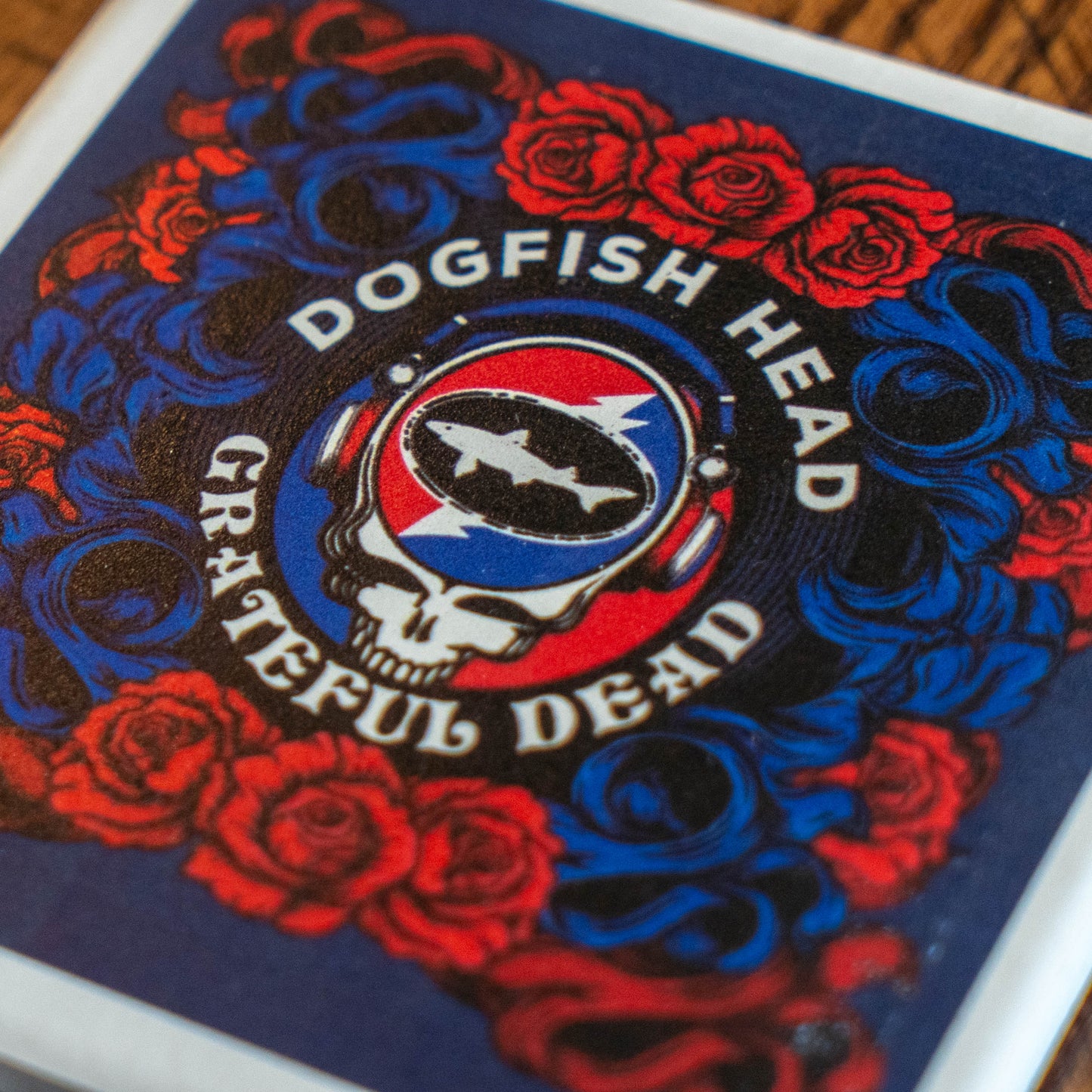 A close-up of a square coaster featuring the Grateful Dead 'Dogfish Head' graphic, with red roses and blue and black swirling patterns on a dark background.
