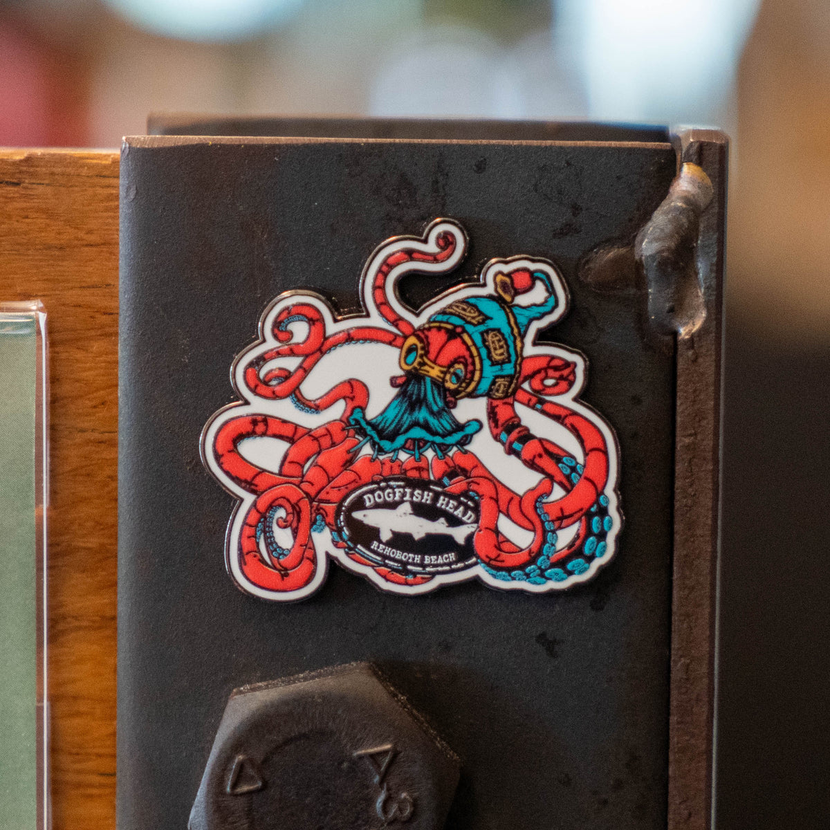 A Kraken Enamel Magnet shaped like a red kraken wearing a blue diving helmet, featuring a logo that reads Rehoboth Beach in the center.
