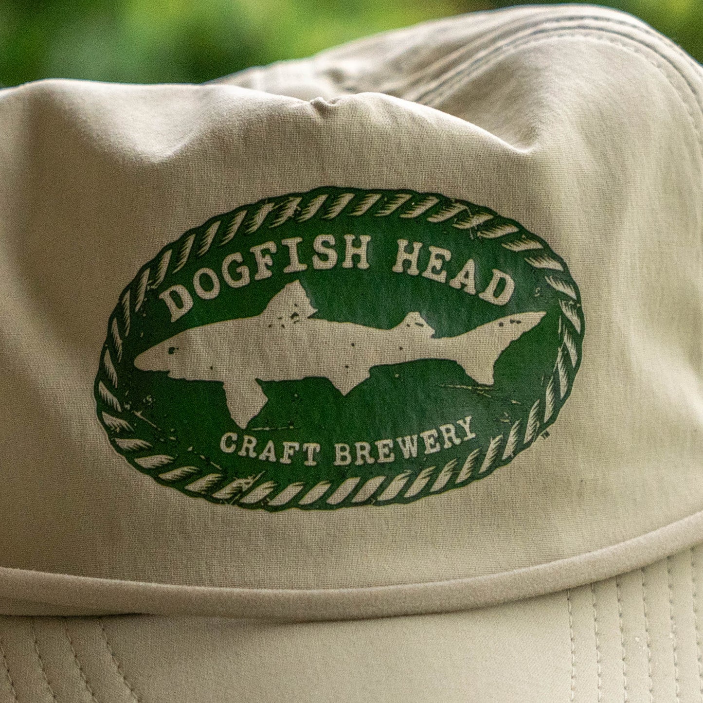 Close up of Green dogfish head craft brewery logo styled with rope borders on a tan cap