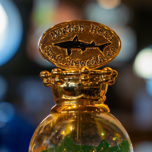 A close-up of the OG Uber Tap Handle by Taphandles Inc., displaying a detailed shark logo and "Dogfish Head Craft Brewed Ales," set against a blurred, colorful background.