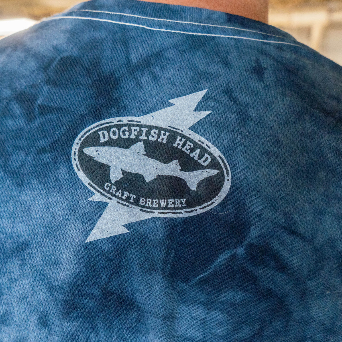Navy Dogfish Head x Grateful Dead Navy Tie Dye Short Sleeve Tee Shirt featuring a white graphic on the back of a shark inside an oval and Dogfish Head Craft Brewery text layered over a lightning bolt.