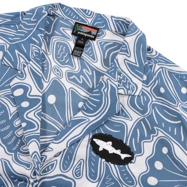 A close-up of the Patagonia W Blue Threads Button Up, a women’s blue and white patterned shirt with abstract shapes and dots, featuring a black and white bat patch on the chest.