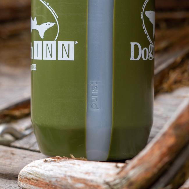 A close-up of the BPA-free olive green INN Water Bottle by Specialized, featuring a gray vertical stripe labeled "purist," resting on weathered wood outdoors at Dogfish Head INN.