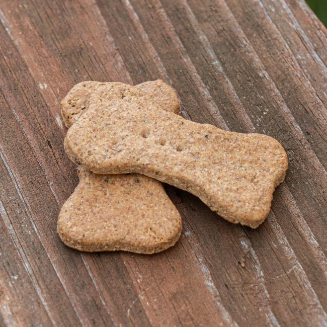 Two Waggies 2-Pack Dog Treats by Waggies by Maggie & Friends Inc, shaped like bones, are stacked on a weathered wooden surface.