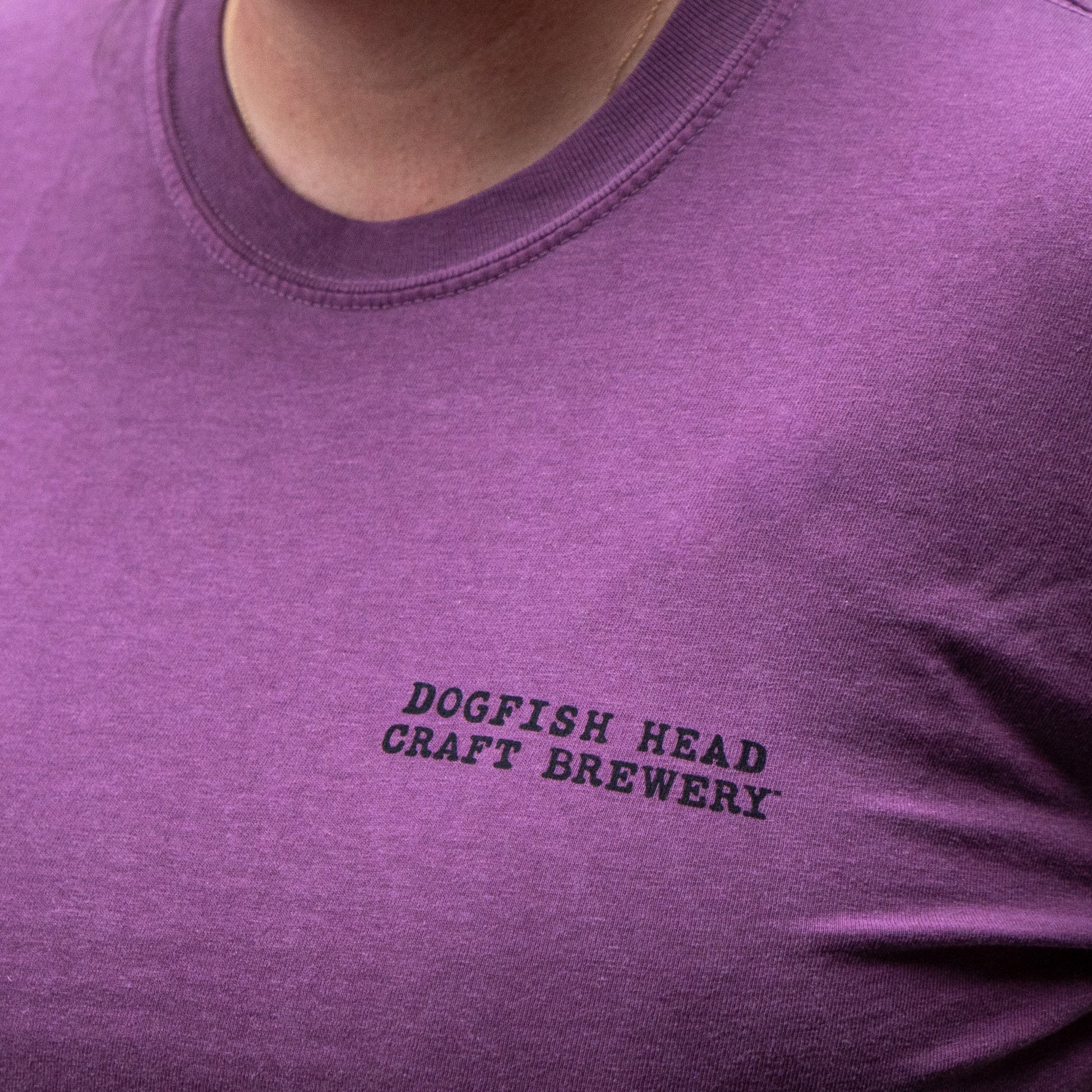 Close-up of a person wearing the GO WEST T-SHIRT COMPANY Berry Oversize Logo Long Sleeve, a relaxed-fit purple shirt with a logo on the chest.