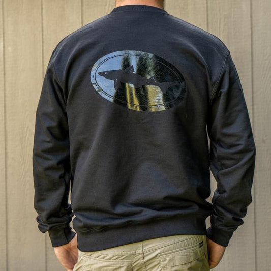 A person faces away wearing the Black Off Centered Crew Sweatshirt by GO WEST T-SHIRT COMPANY, made from a soft cotton-polyester blend and featuring a shiny oval Dogfish Head Logo on the back, standing before a wooden wall.
