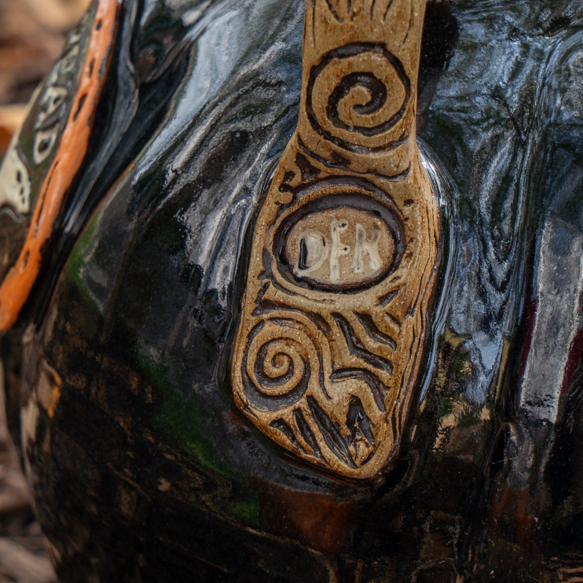 A close-up of the Black Punkin Growler by Romanick Pottery: a glossy, dark ceramic vessel with a tan textured handle, intricate swirl carvings, and “DEN” engraved at the center—one of our limited edition growlers.
