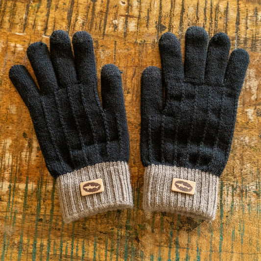 A pair of Black and Tan Gloves by Arrasmith Promotions LLC with gray ribbed cuffs and small brown fish logo patches, displayed on a rustic wooden surface.