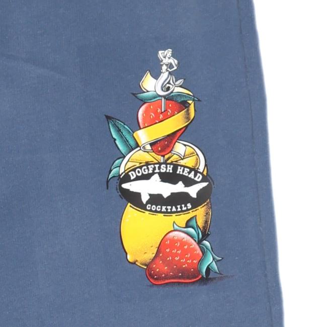 A yellow cocktail glass with lemon, strawberries, green leaves, and a silver anchor graphic sits on dark blue fabric—ideal for pairing with cozy Blue Mermaid Sweatpants by GO WEST T-SHIRT COMPANY. The black label displays Dogfish Head Cocktails in white text.