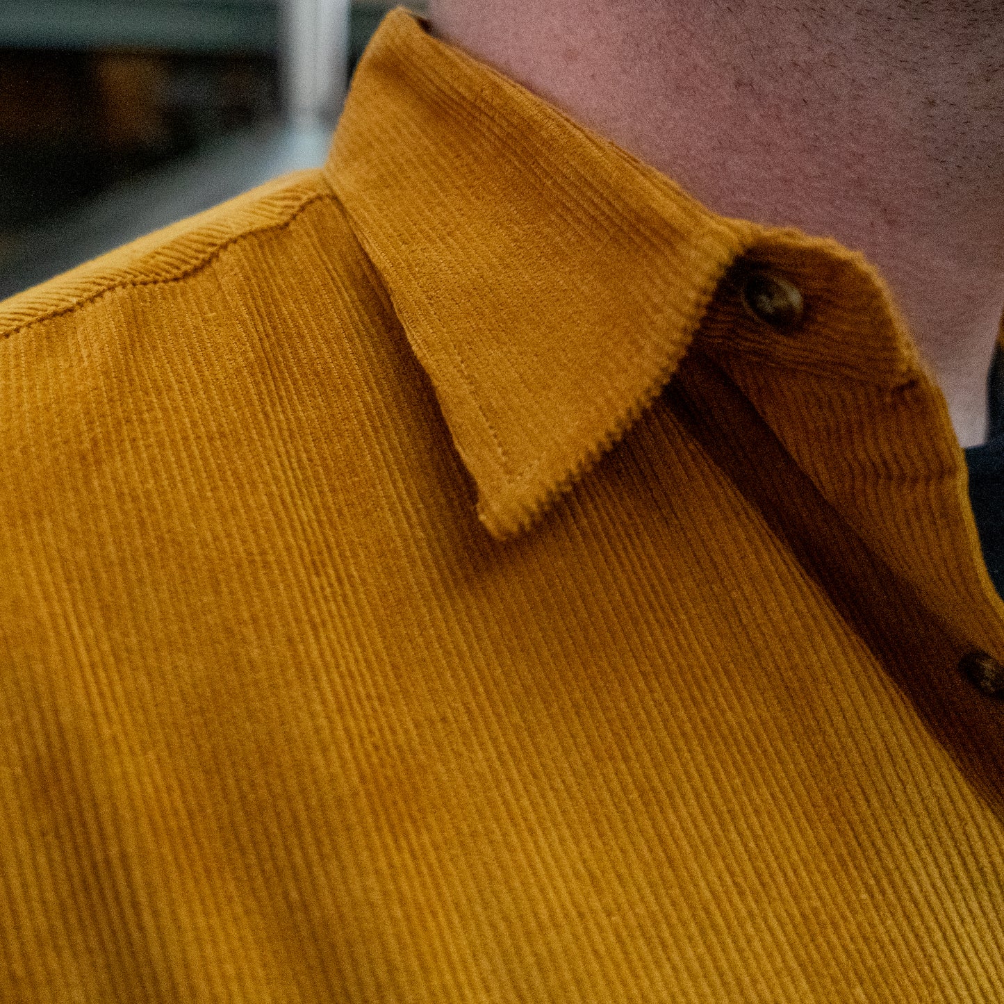 Close-up of a person wearing the Camel Cord Flannel Button Down by Brewery Branding, Inc., highlighting the collar and top shoulder in camel tones against a blurred background.