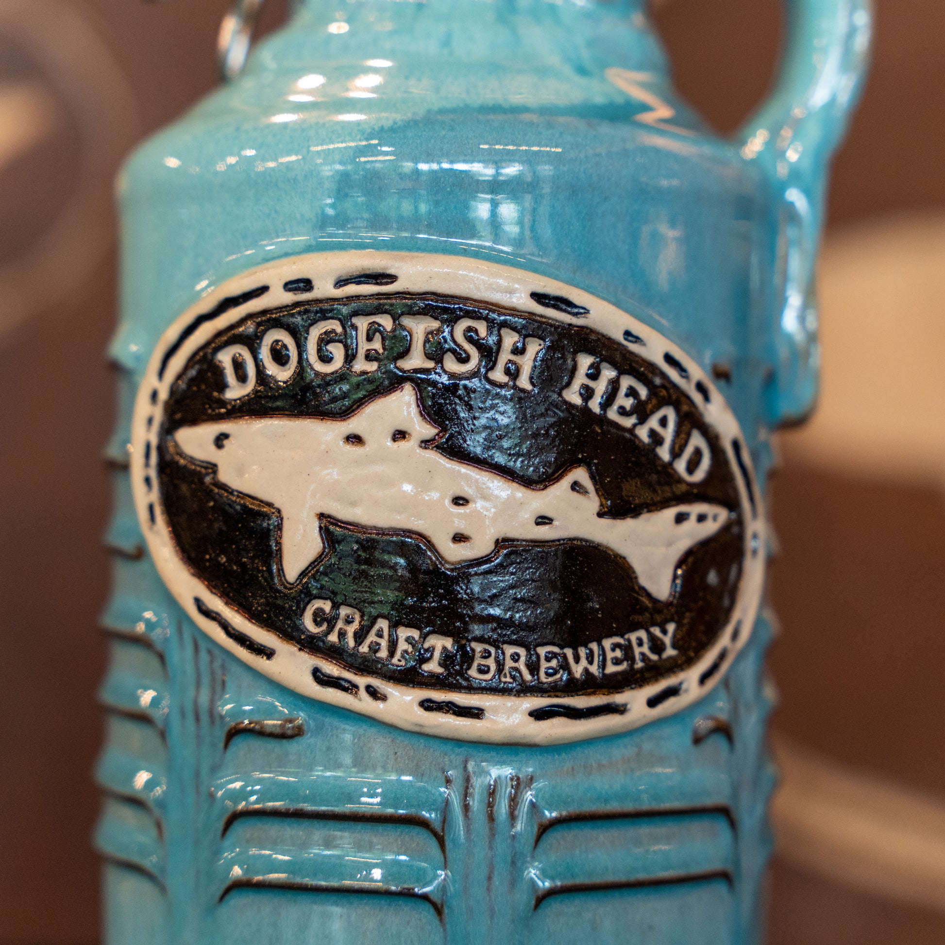 A close-up of the Coastal Blue Ceramic Growler by Romanick Pottery shows a hand crafted design with an embossed oval label featuring a white shark.