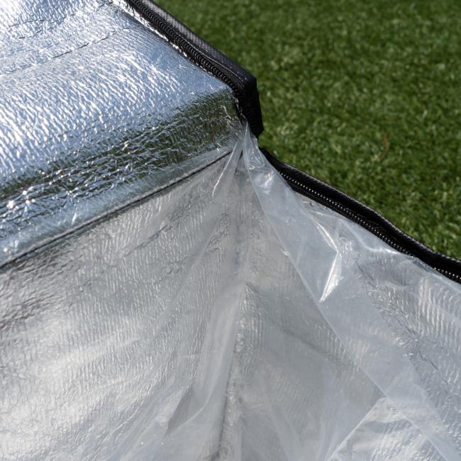 A close-up of the Go Match Up Cooler Bag shows its insulated, reflective silver-lined interior with a clear plastic liner, set on green grass.
