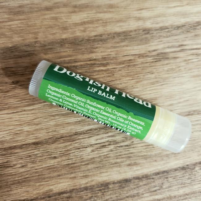 A tube of DFH Lip Balm by Eco Lips Inc with a green label rests on wood, featuring organic sunflower oil, beeswax, coconut oil, and essential oils for a refreshing organic experience.