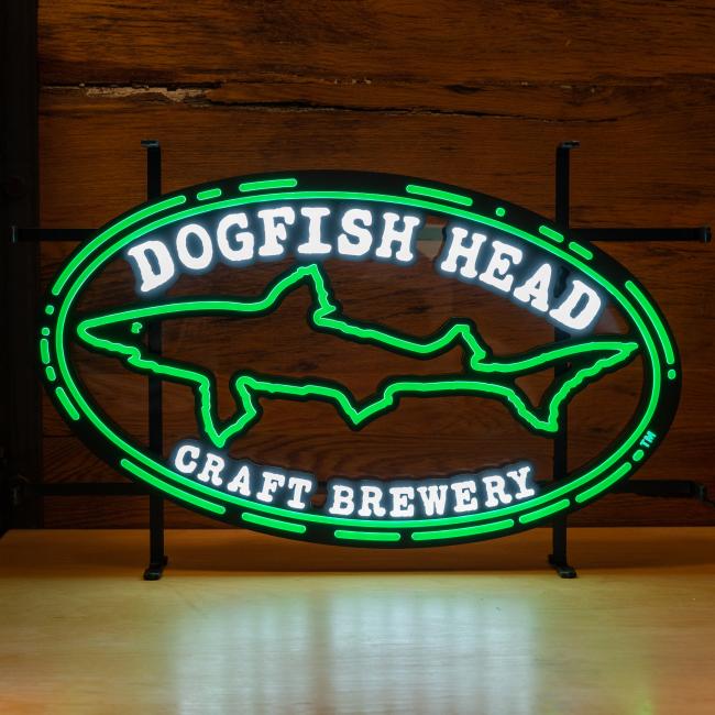 The Merchtank DFH Craft Brewery LED Neon features a glowing shark outline and "Dogfish Head Craft Brewery" text in white with a green border, creating a striking display against wooden backdrops.