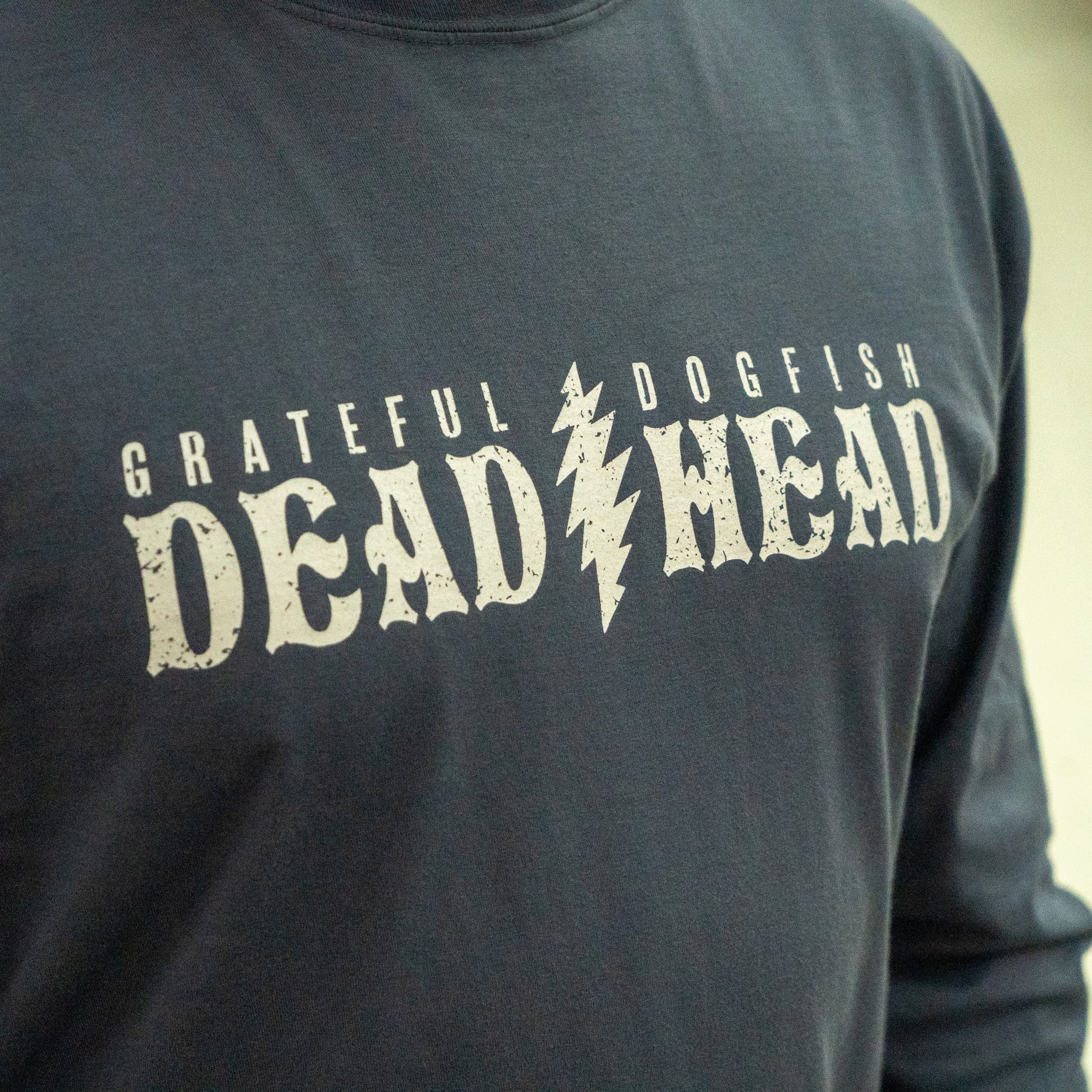 A close-up of the Dogfish Head x Grateful Dead Anchor Slate Long Sleeve Tee by GO WEST T-SHIRT COMPANY, showing "GRATEFUL DOGFISH DEAD HEAD" in distressed white with a lightning bolt—a must-have for fans of both brands.