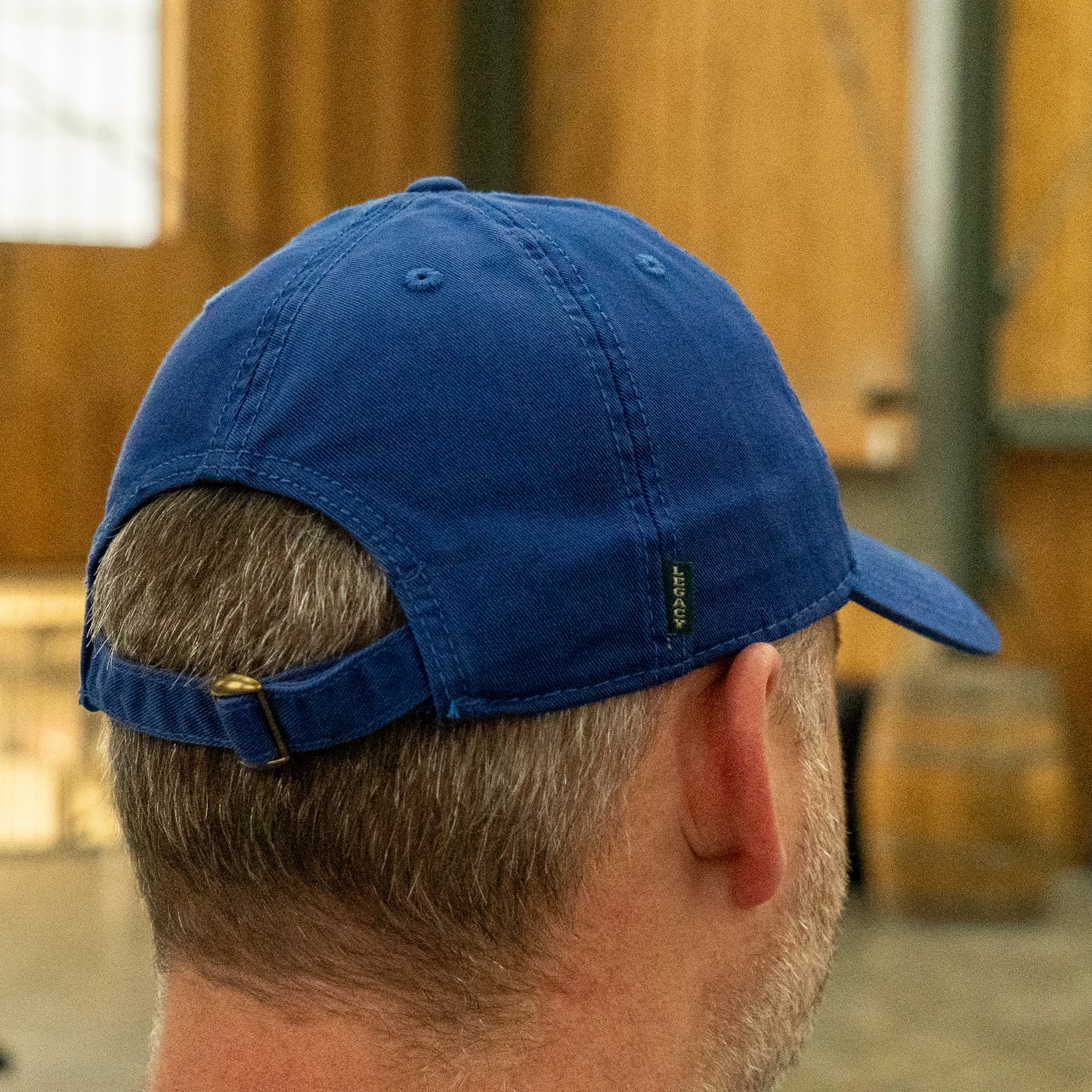 A person wearing the Dogfish Head x Grateful Dead LEGACY Royal Dad Hat by L2 Brands, with an adjustable strap, is seen from behind in a wooden interior—an ideal gift for beer lovers and brewery enthusiasts.