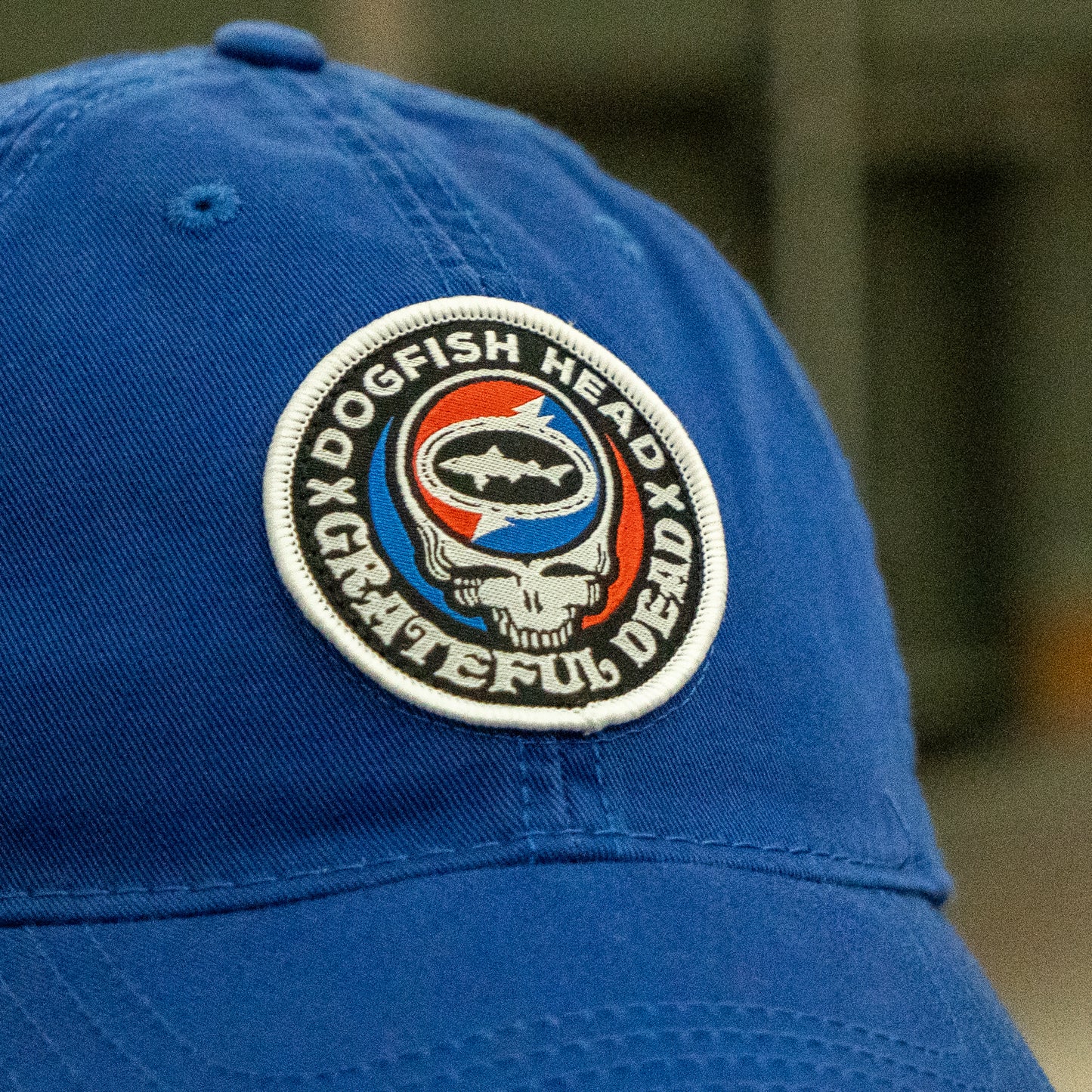 Close-up of the Dogfish Head x Grateful Dead LEGACY Royal Dad Hat by L2 Brands, featuring a round patch with “Dogfish Head Grateful Dead,” a shark logo, and a skull in red, white, and blue—perfect for beer lovers gifts.