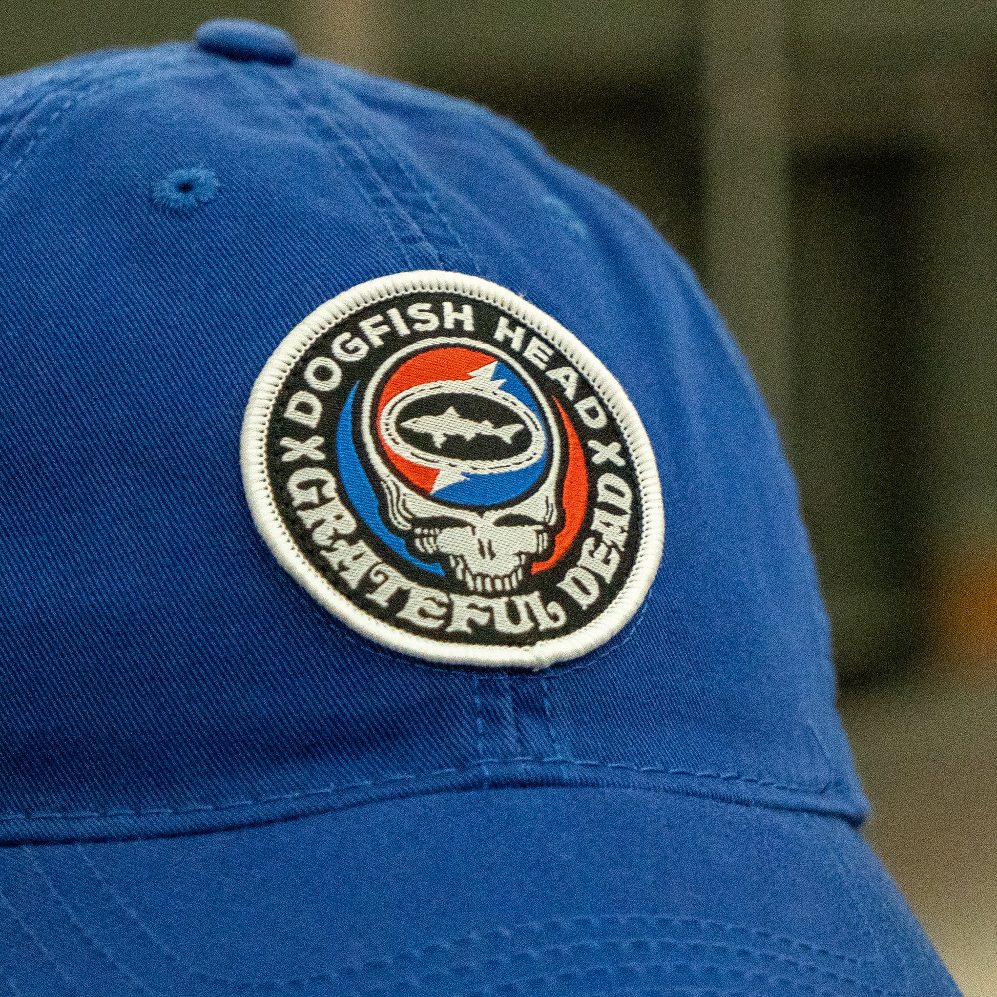 Close-up of the Dogfish Head x Grateful Dead LEGACY Royal Dad Hat by L2 Brands, featuring a round patch with “Dogfish Head Grateful Dead,” a shark logo, and a skull in red, white, and blue—perfect for beer lovers gifts.