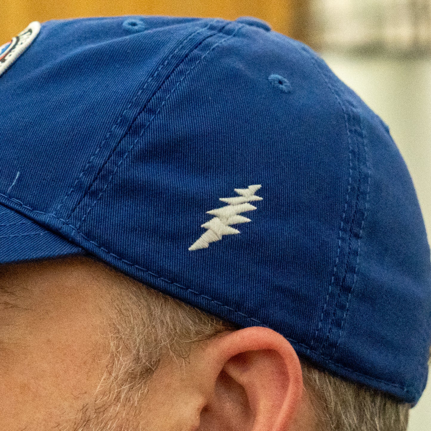 Close-up of a person wearing the Dogfish Head x Grateful Dead LEGACY Royal Dad Hat by L2 Brands, featuring a blue design and white embroidered lightning bolt—an ideal gift for beer lovers.