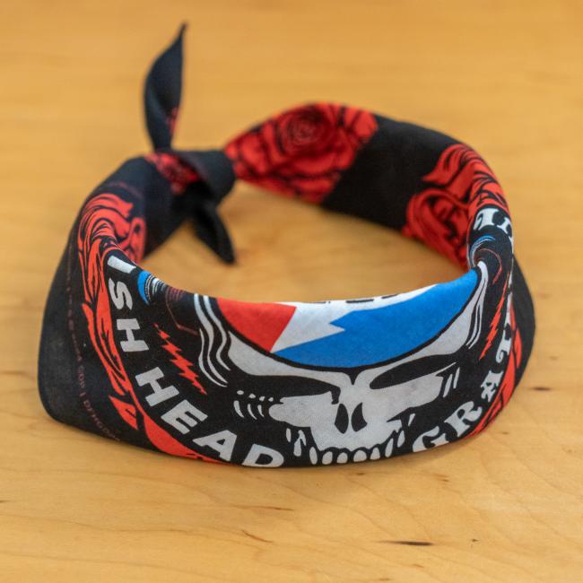 The Dogfish Head x Grateful Dead Bandana by Merchtank, with black fabric and red, white, and blue skull and roses design, is tied in a loose knot on a wooden surface—an ideal craft beer accessory.