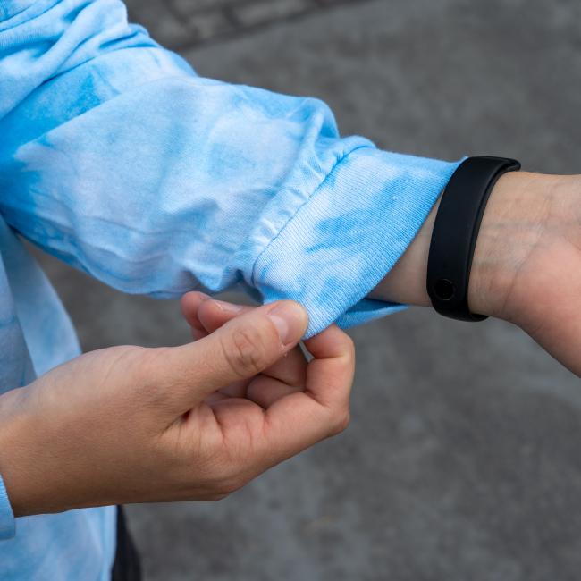 Wearing the Dogfish Head x Grateful Dead Blue Tie Dye Long Sleeve Tee by GO WEST T-SHIRT COMPANY, someone rolls up their sleeve to reveal a black fitness tracker, with a relaxed outdoor backdrop capturing the tee’s adventurous spirit.