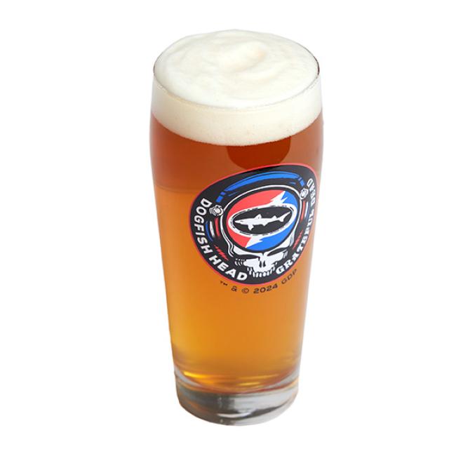 The Dogfish Head x Grateful Dead Glass by Grandstand Glassware & Apparel features a vibrant shark and lightning bolt design—perfect for craft beer lovers enjoying an amber pint with a thick foam head.
