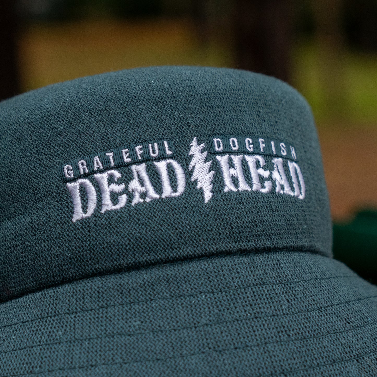Close-up of the Dogfish Head x Grateful Dead KANGOL Bucket Hat by BOLLMAN HATS in green, with "GRATEFUL DOGFISH DEAD HEAD" embroidered in white and a lightning bolt symbol between "DEAD" and "HEAD.
