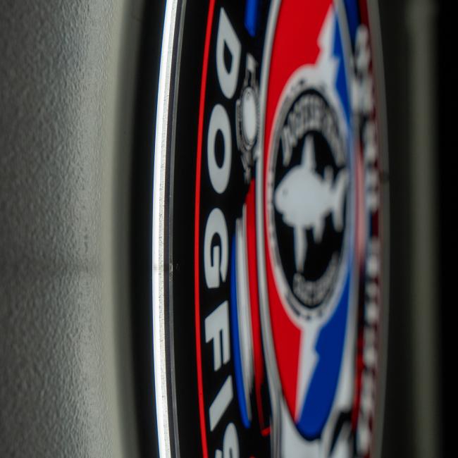 Close-up of the Firebolt Group Dogfish Head x Grateful Dead LED sign on a wall, featuring a red, blue, and black shark logo and "DOGFISH" text. Slightly blurred for unique bar decor appeal.
