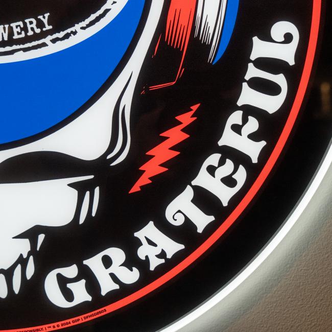 A close-up of the Firebolt Group Dogfish Head x Grateful Dead LED Sign shows "GRATEFUL" in bold white on black, with a red lightning bolt and part of a stylized hand—an ideal bar decor piece.