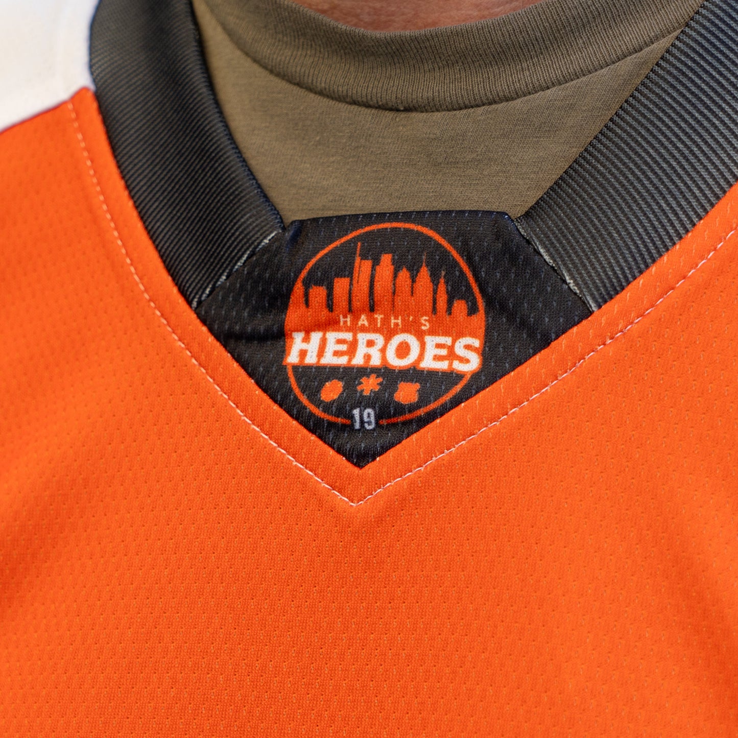 Close-up of the collar on the Dogfish Head x Garnet Hathaway Engine 19 Hockey Jersey by In Your Face Apparel, featuring a black HATHS HEROES patch with a city skyline, snowflake, and hockey puck to honor first responders.
