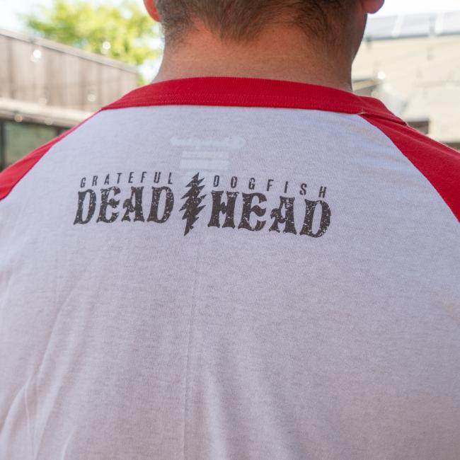 The back of the white tee with red sleeves. Under the neck, "Grateful Dead " and "Dogfish Head" is written with a lightning bolt in between them.