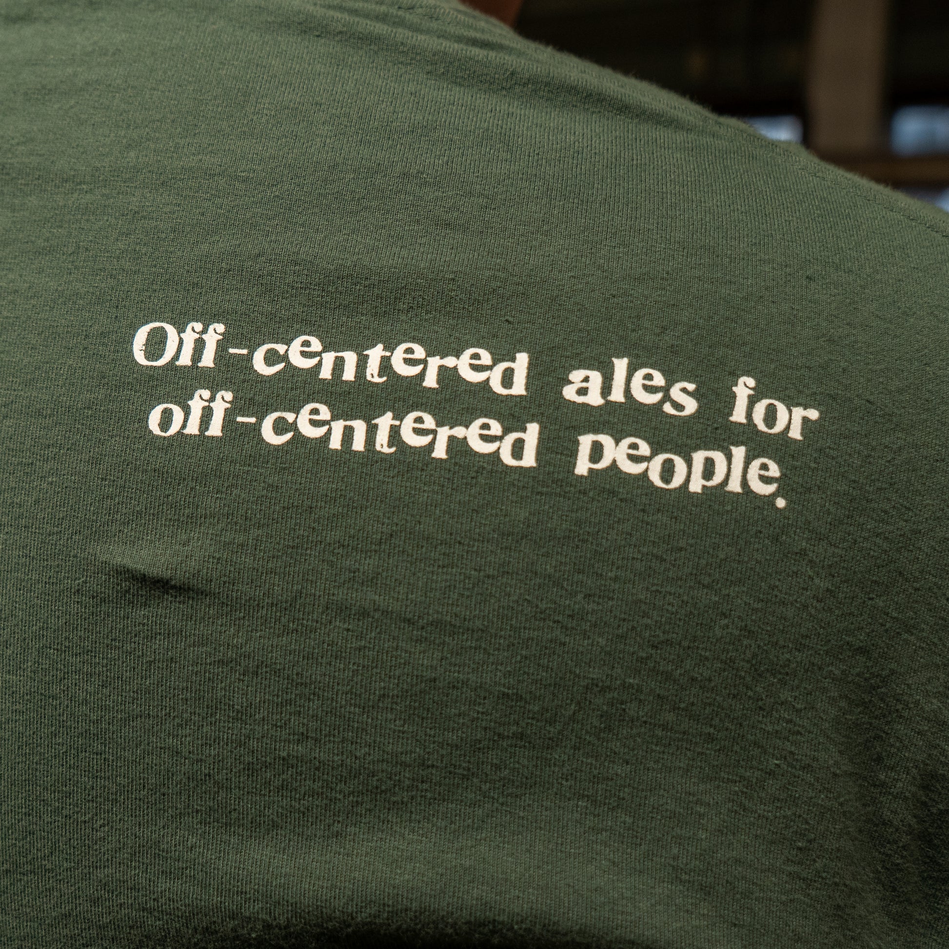 The Green Since 95 Short Sleeve Logo Tee by GO WEST T-SHIRT COMPANY is a soft, green cotton shirt featuring "Off-centered ales for off-centered people" in white text on the back.