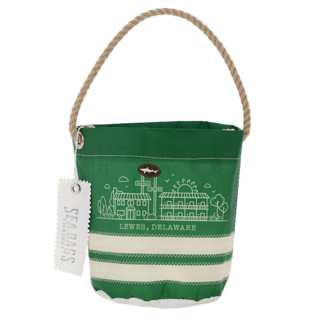 The INN Seabag Bucket Bag by Seabags is handcrafted in Maine from recycled sail material. It features a green design, rope handle, white Lewes, Delaware landmark drawings, and a “Seabags” tag attached to the handle.