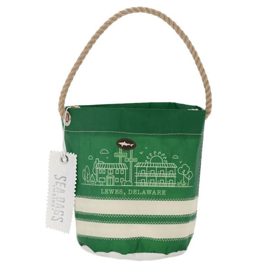 The INN Seabag Bucket Bag by Seabags is handcrafted in Maine from recycled sail material. It features a green design, rope handle, white Lewes, Delaware landmark drawings, and a “Seabags” tag attached to the handle.