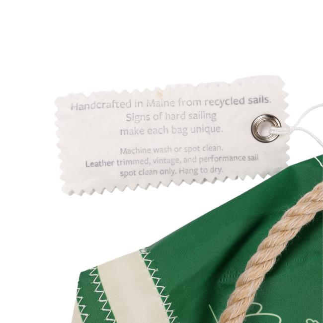 A close-up of the Seabags INN Seabag Bucket Bag with a thick rope handle. A scalloped tag reads, “Handcrafted in Maine from recycled sails. Signs of hard sailing make each bag unique.”.