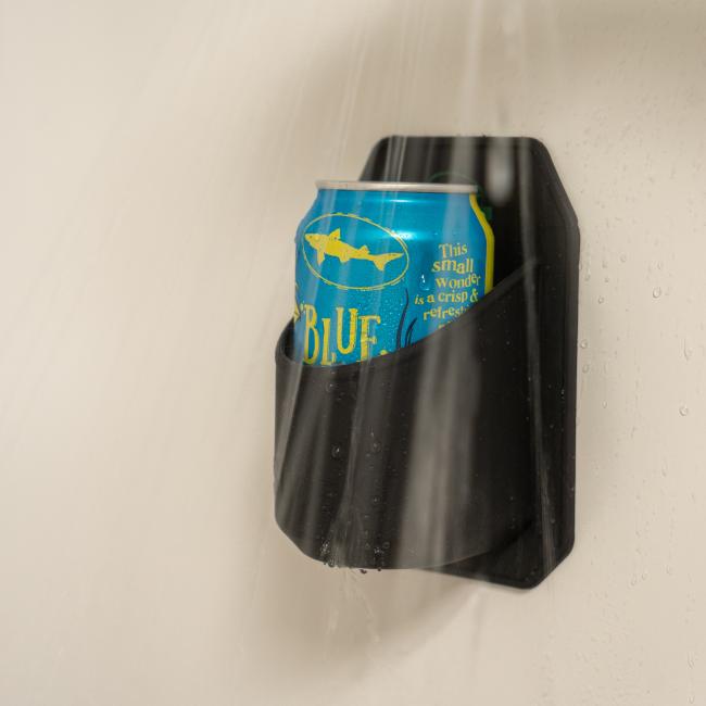 A blue soda can rests in the Sudski INN Shower Beer Holder, securely mounted on the wall with water streaming down—ideal for relaxing showers or as a fun beer gift.