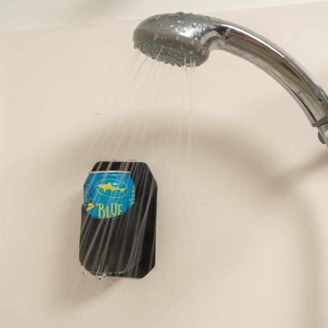 A can of Dogfish Head Blue Hen beer sits in the wall-mounted black INN Shower Beer Holder by Sudski as water sprays from a running showerhead above.