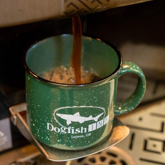 A dark green Inn Camp Cup by Grandstand Glassware & Apparel is being filled with coffee from a dispenser, forming foam as it pours in. The 12oz mug sits on a metal tray.