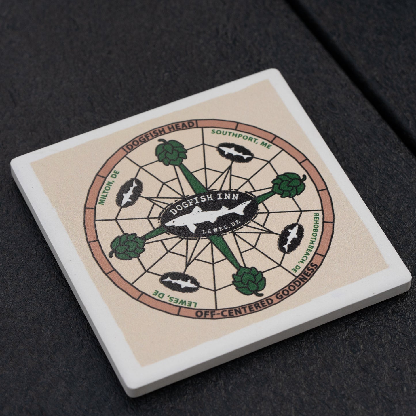 The Inn Ceramic Off Centered Coaster by Paint the Town, Inc. features a compass motif with Dogfish Inn at the center, directions to Lewes, Milton, Dogfish Head, and Southport, plus hop icons—ideal for your next craft beer adventure.