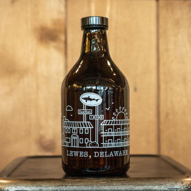 The 32oz Inn Growler by Grandstand Glassware & Apparel features white illustrations of local Lewes, DE architecture, the Dogfish Head logo, and INN details. Shown on a metal surface with a wood background.