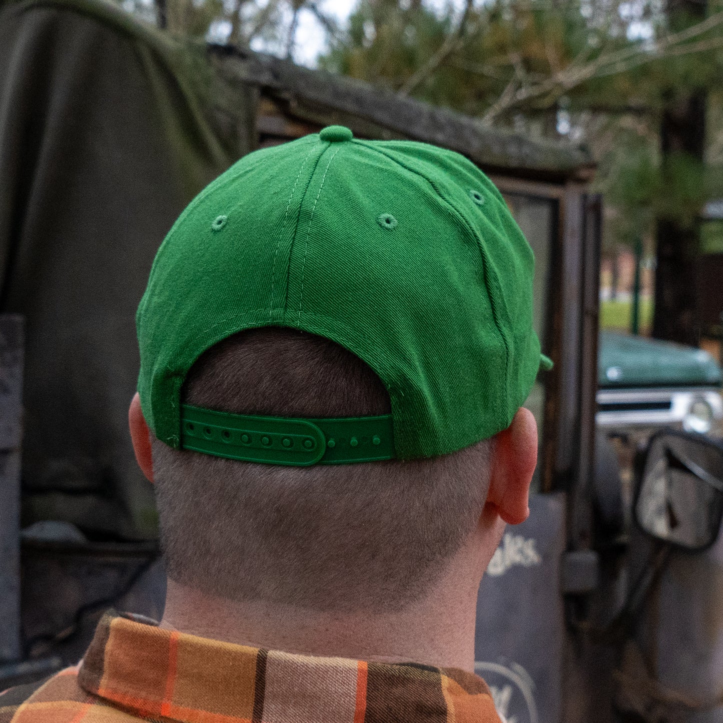 A person wearing a Merchtank Kelly Green Rope Hat is seen from behind, standing outdoors near a vehicle with trees in the background.