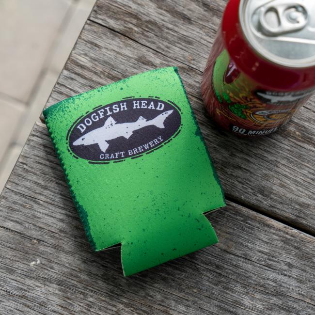 A Merchtank Lime Green Craft Brewery 12oz Can Cooler sits on a weathered wooden surface next to an opened red beverage can.
