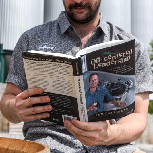 Outdoors, a person in a patterned short-sleeve shirt reads Book- Off-Cent Leadership by J Wiley and Sons Publishing, showing both the front and back covers.