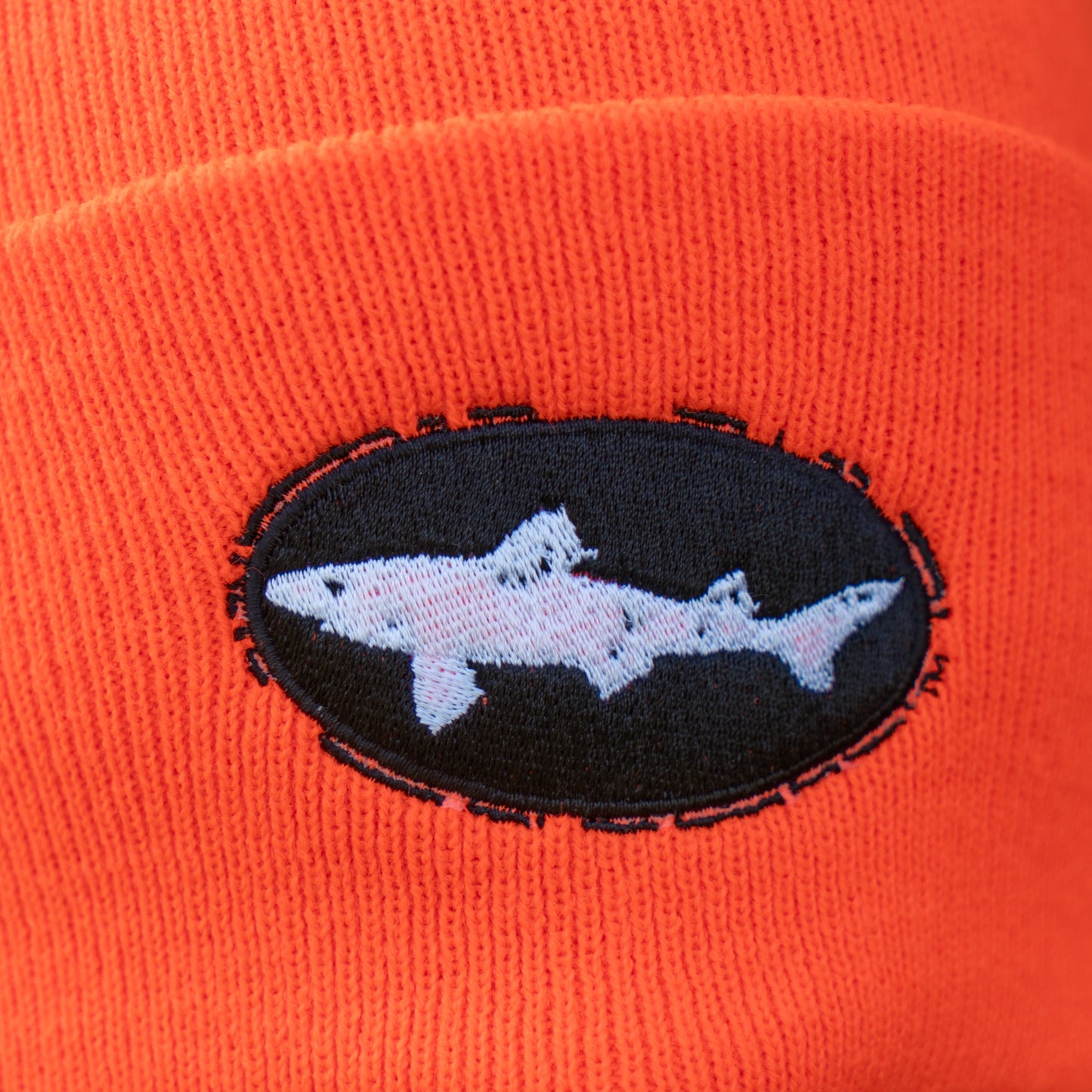 Close-up of the Orange Carhartt Beanie by Mirror Image Inc., showcasing an embroidered patch with a white shark silhouette inside a black oval—ideal for staying warm in style.