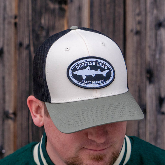 Man looking down wearing a black and white Dogfish Head trucker hat with an olive colored rim. The mesh on the back half is black and the front is solid white with a black dogfish head craft brewery logo.